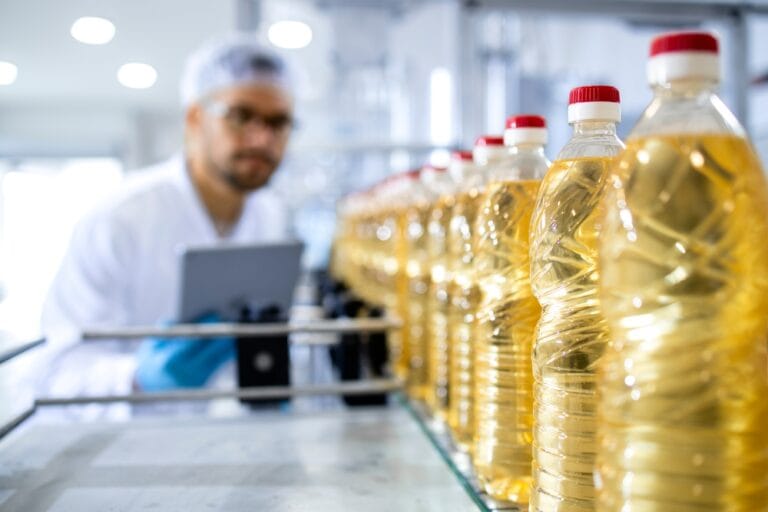 Bottles of seed oil in a production line with a technician inspecting the process, symbolizing the role of seed oils in modern diets.