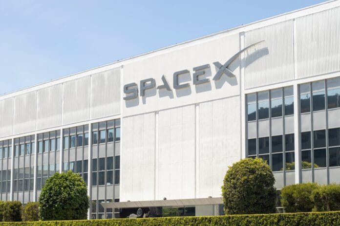 SpaceX headquarters building with its logo prominently displayed on the facade, surrounded by green landscaping.