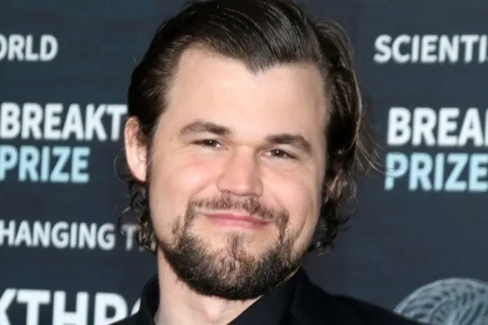 Magnus Carlsen smiling at the Breakthrough Prize event, wearing a black suit, known for his chess achievements and the #JeansGate controversy.