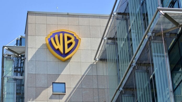 Warner Bros. logo on the exterior of a modern office building, featuring the iconic WB shield in blue and gold against a light stone facade