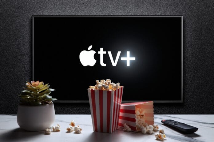 Apple TV+ logo displayed on a screen with a popcorn bucket, a remote control, and a small plant on a table in front of it.