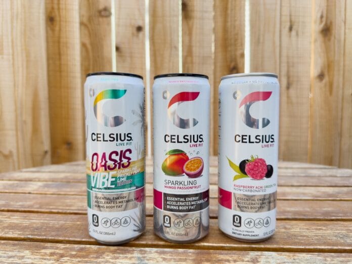 Three Celsius energy drink cans on a wooden table with a wooden fence background.