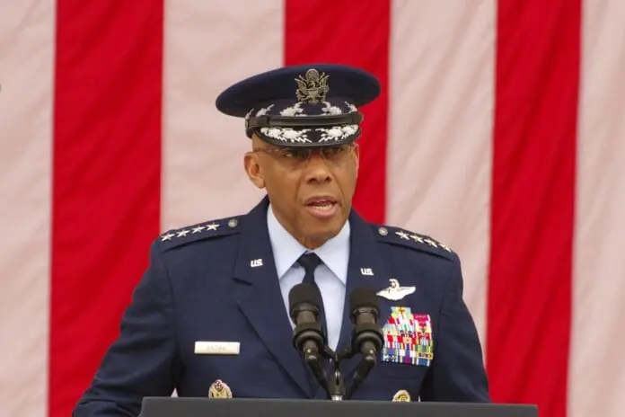 A high-ranking U.S. military officer in full dress uniform delivers a speech at a formal event, standing in front of an American flag.