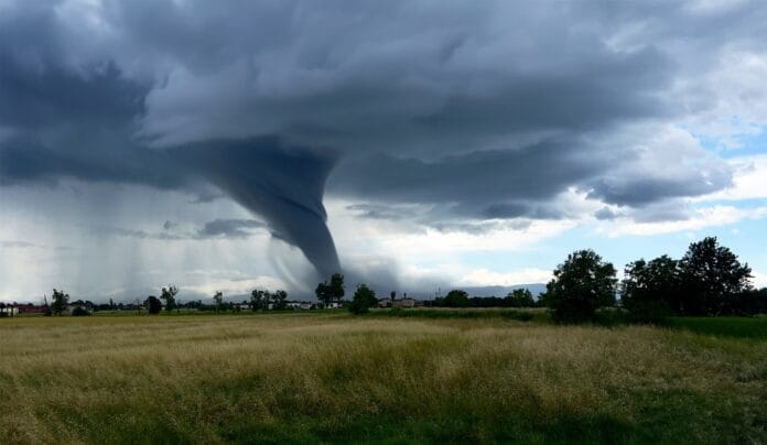 A powerful tornado forming in an open field under dark storm clouds.