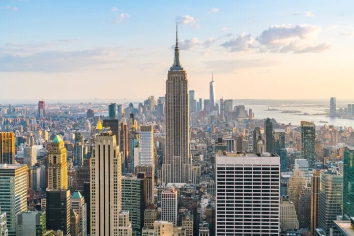 A panoramic view of the New York City skyline featuring the Empire State Building and surrounding skyscrapers at sunset.