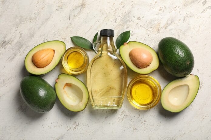 A bottle of avocado oil surrounded by fresh avocados and small bowls of oil, showcasing its health benefits and versatility in cooking and skincare.