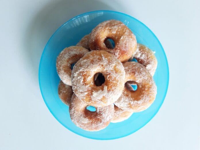 A plate of powdered sugar donuts stacked on a blue dish.