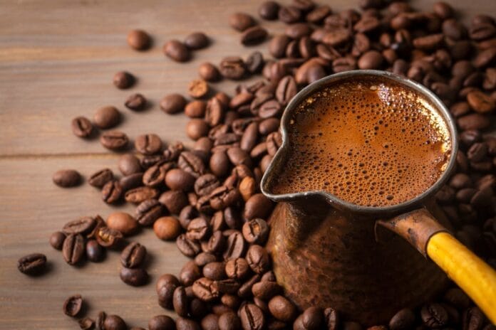 A traditional Turkish coffee pot filled with rich, foamy coffee surrounded by roasted coffee beans on a wooden surface.