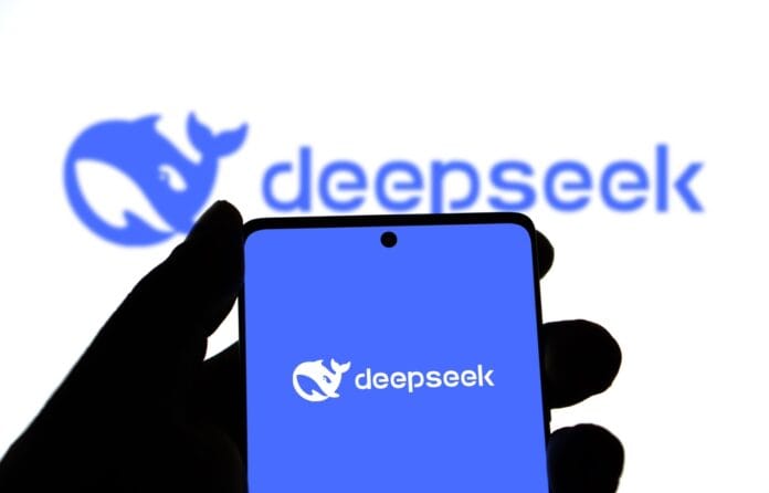 A silhouette of a hand holding a smartphone displaying the DeepSeek logo, with the logo also visible in the background.